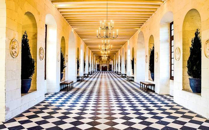 Grand hallway with checkered floor and chandeliers at Château de Chenonceau, France.