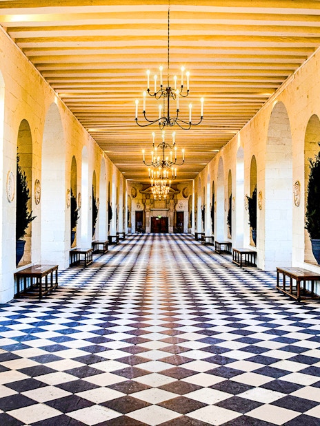 Grand hallway with checkered floor and chandeliers at Château de Chenonceau, France.
