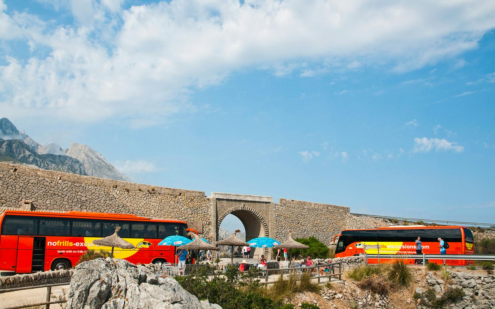 Mallorca sightseeing tour buses near stone archway with mountains in background.