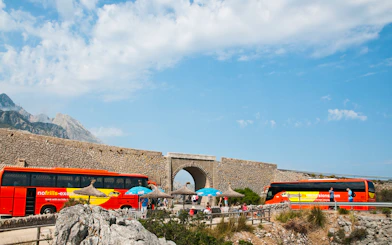 Mallorca sightseeing tour buses near stone archway with mountains in background.