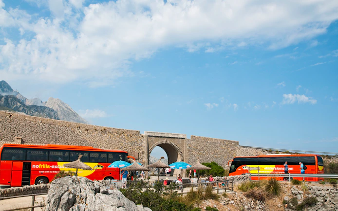 Mallorca sightseeing tour buses near stone archway with mountains in background.
