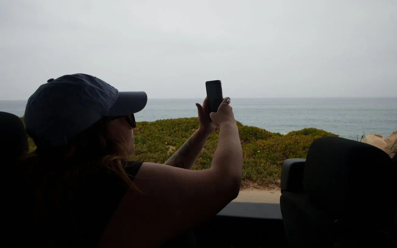 Person taking a photo of the ocean view from a vehicle on the Pacific Coast Highway tour.