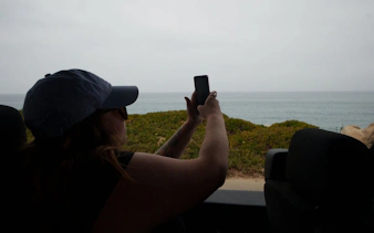Person taking a photo of the ocean view from a vehicle on the Pacific Coast Highway tour.