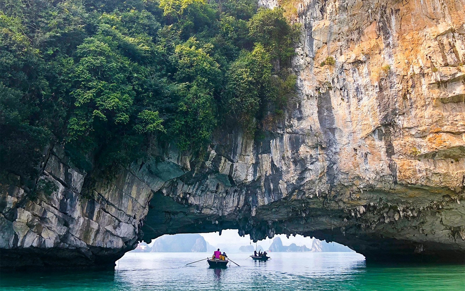 Kayakers explore limestone arch in Halong Bay on Dragonfly Cruise tour.
