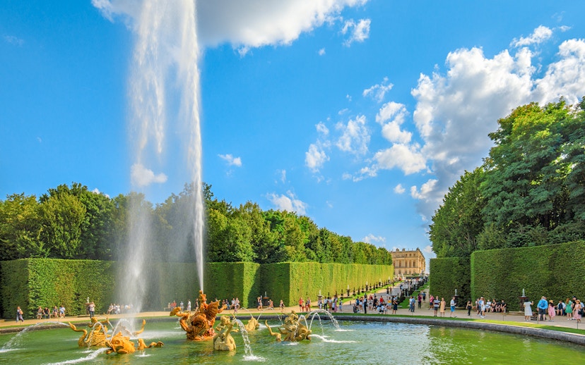 Fountain at Dragon Basin, Versailles, with visitors and palace in background.