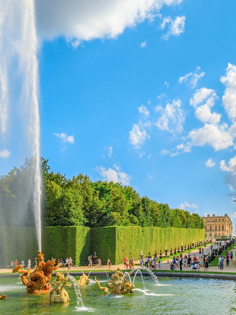 Fountain at Dragon Basin, Versailles, with visitors and palace in background.