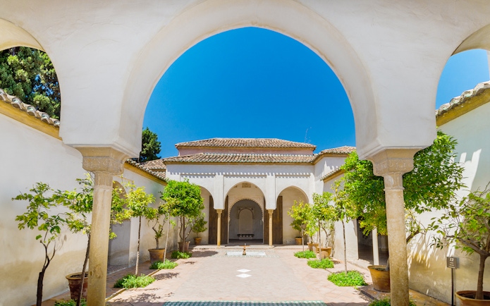 Alcazaba courtyard with arches and potted trees in Malaga, Spain.