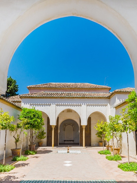 Alcazaba courtyard with arches and potted trees in Malaga, Spain.