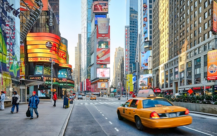 Yellow taxi driving through Times Square, New York City, surrounded by bright billboards and skyscrapers.