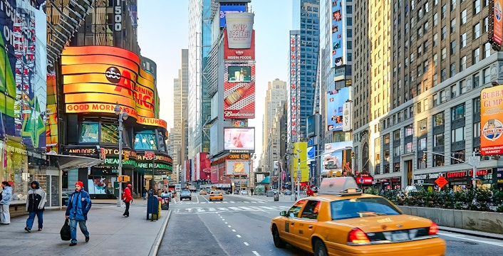 Yellow taxi driving through Times Square, New York City, surrounded by bright billboards and skyscrapers.