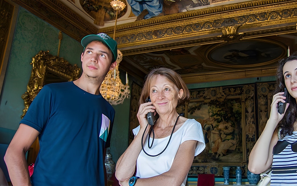 Visitors using audio guides inside Vaux-le-Vicomte, Paris tour.