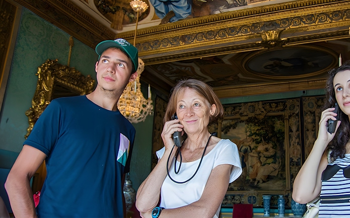 Visitors using audio guides inside Vaux-le-Vicomte, Paris tour.