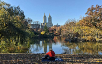 Person sitting by a lake in Central Park with city skyline in the background, New York.