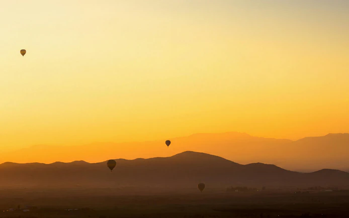 Hot air balloons over Marrakech landscape at sunrise.