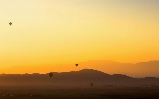 Hot air balloons over Marrakech landscape at sunrise.
