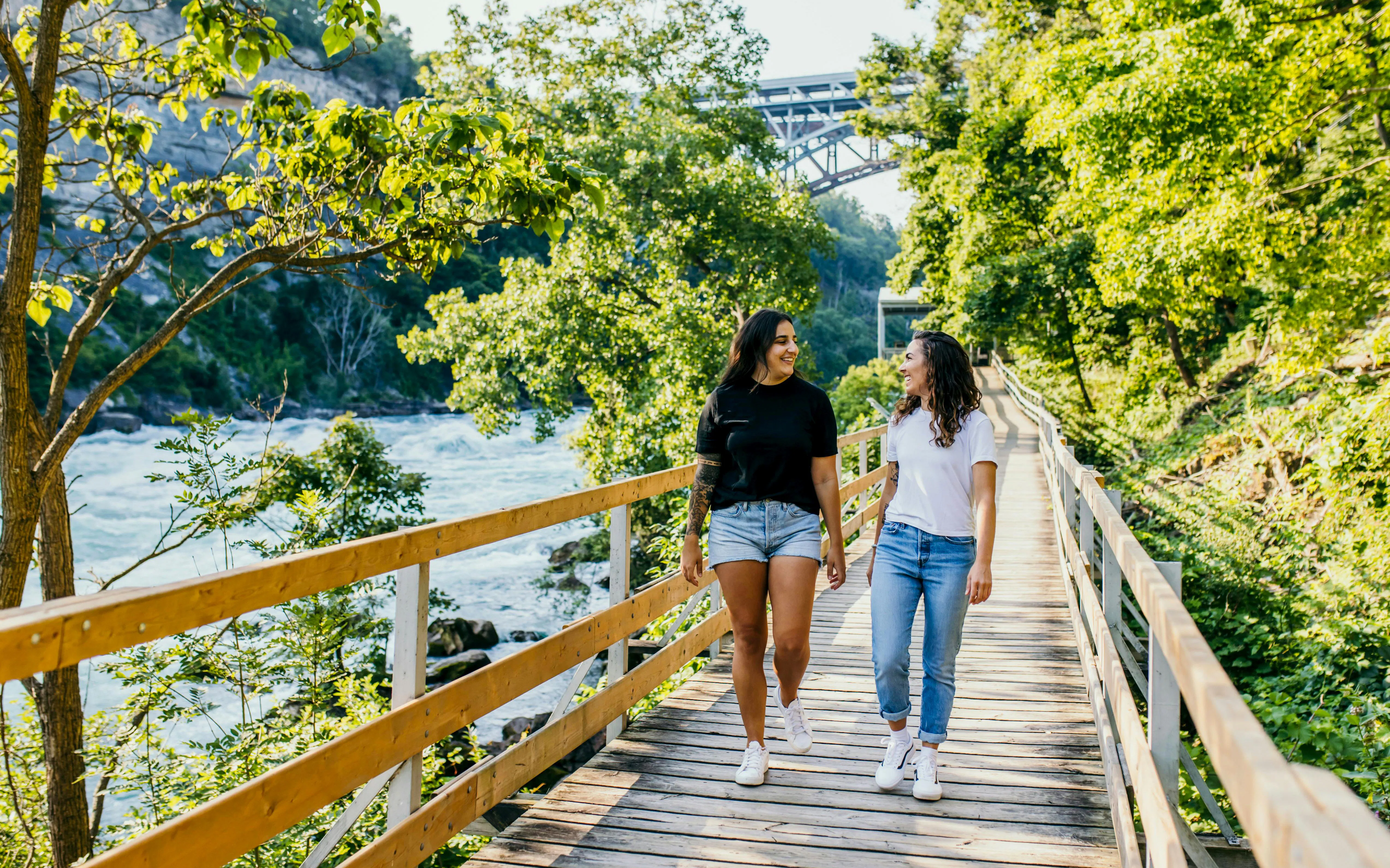 Visitors walking along a wooden boardwalk at White Water Walk, surrounded by lush greenery and river views.