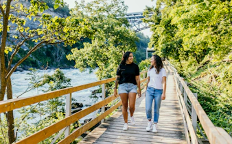 Visitors walking along a wooden boardwalk at White Water Walk, surrounded by lush greenery and river views.