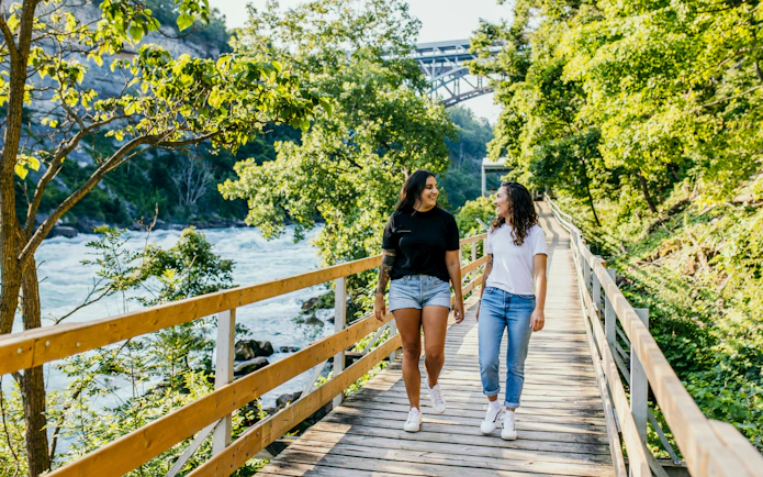 Visitors walking along a wooden boardwalk at White Water Walk, surrounded by lush greenery and river views.