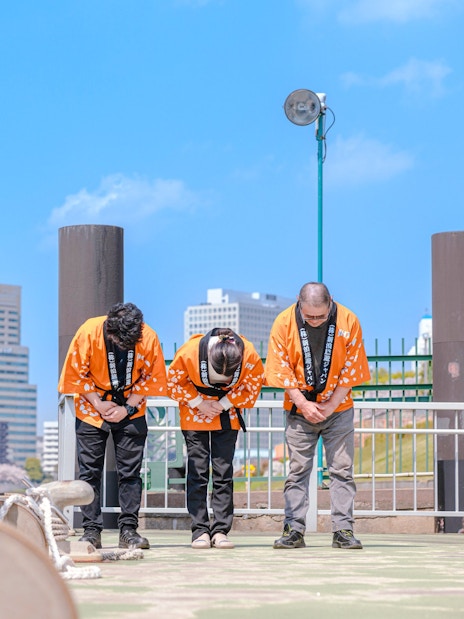 Crew members in traditional attire bowing on the deck of a Yakatabune in Japan.