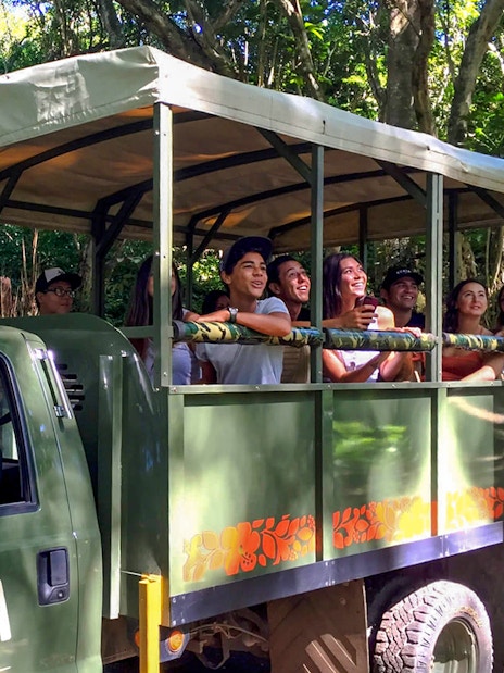 Tourists on an open-air truck exploring lush forest during Jurassic Adventure Tour.