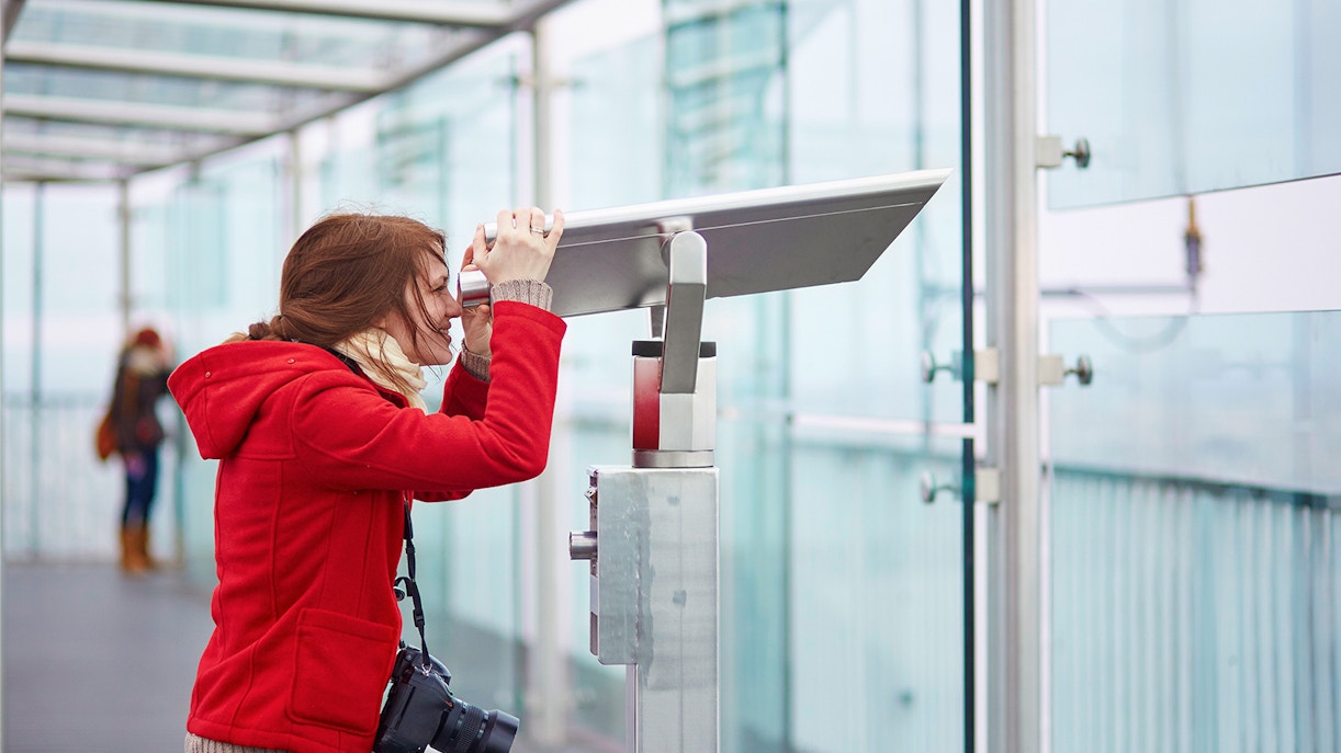 Visitor using telescope on Montparnasse Tower 56th Floor terrace, Paris.