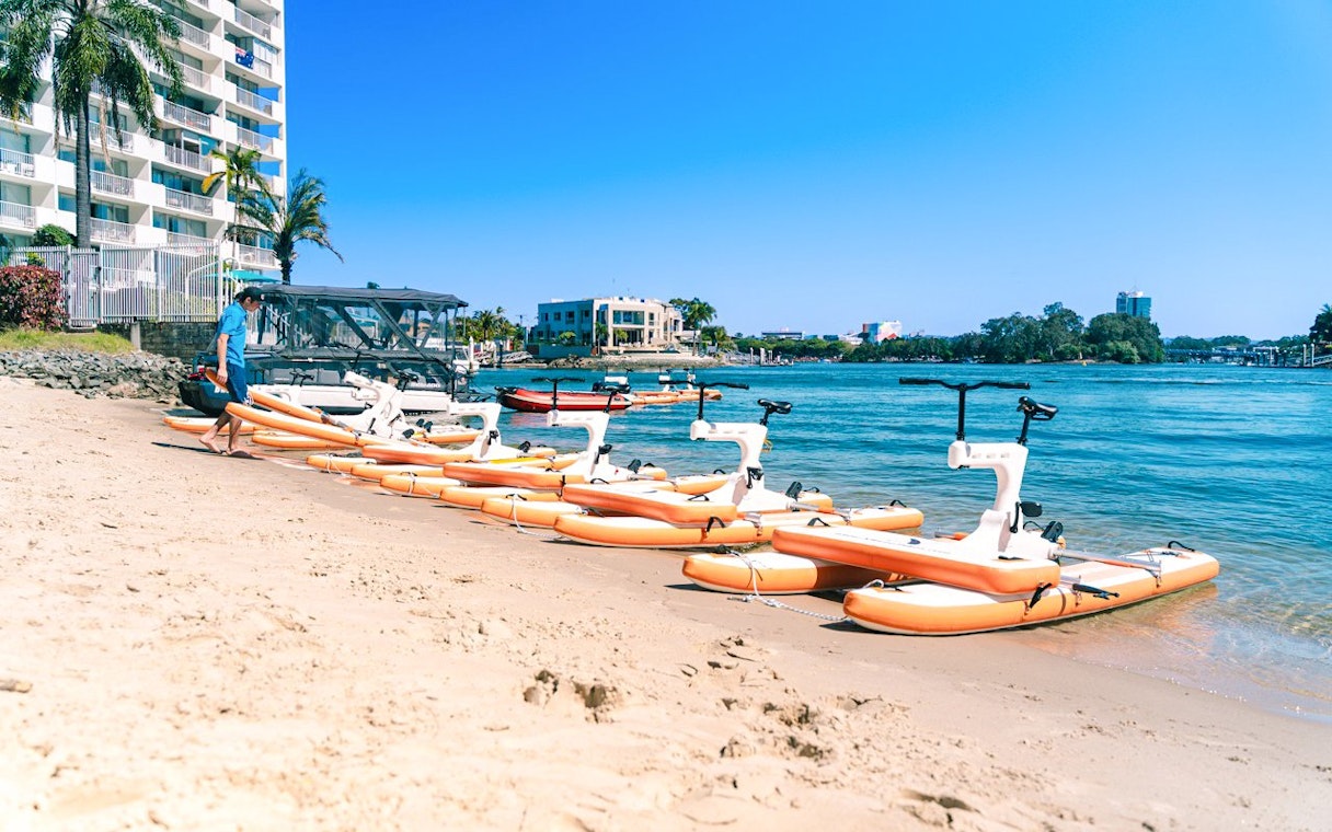 Waterbikes lined up on Gold Coast beach with buildings and water in the background.