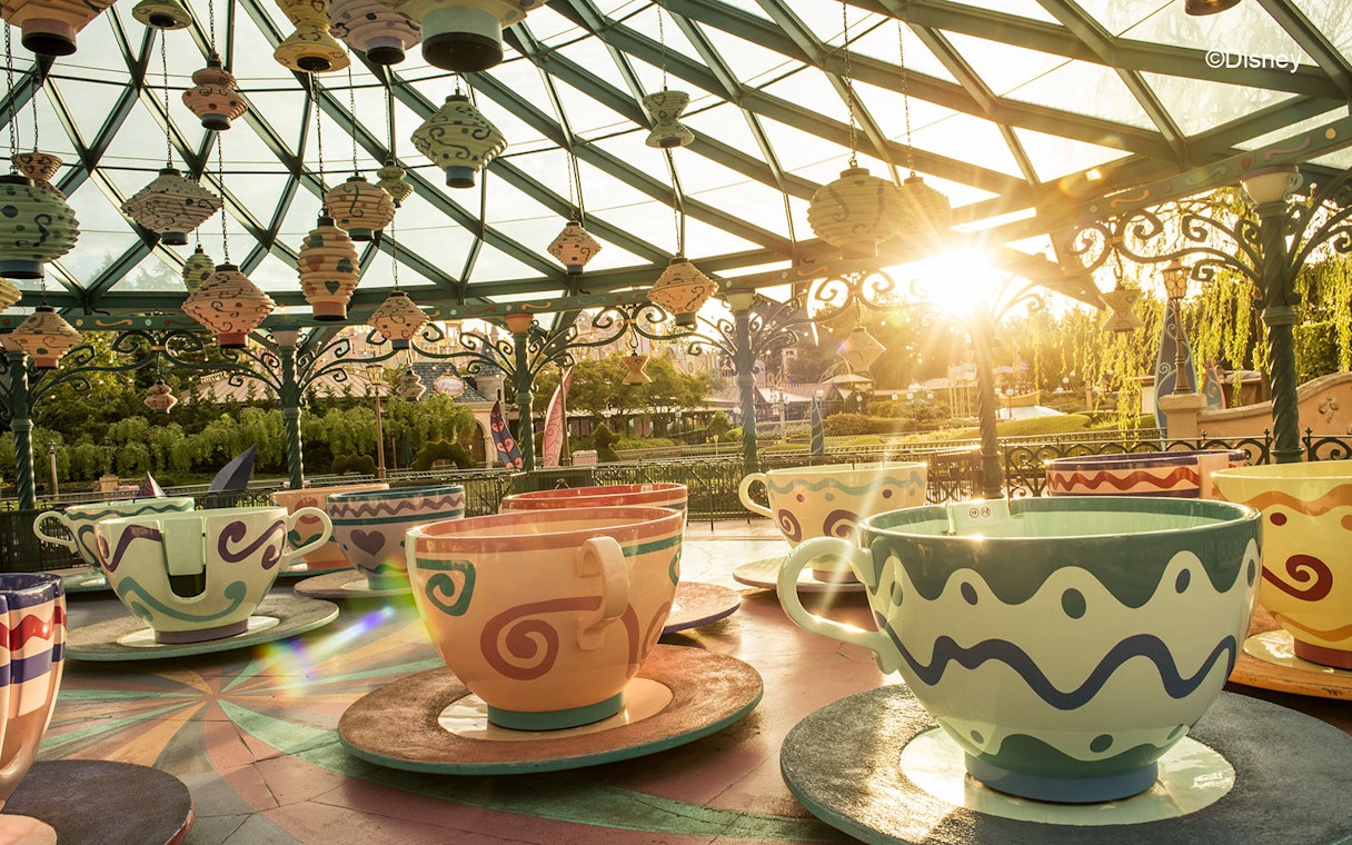 Teacup ride at Disneyland Paris with colorful cups under a glass canopy at sunset.