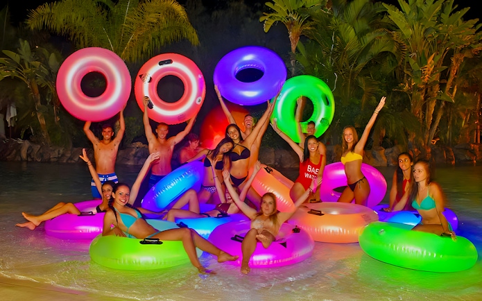 Friends enjoying illuminated float rings at Siam Park at night.
