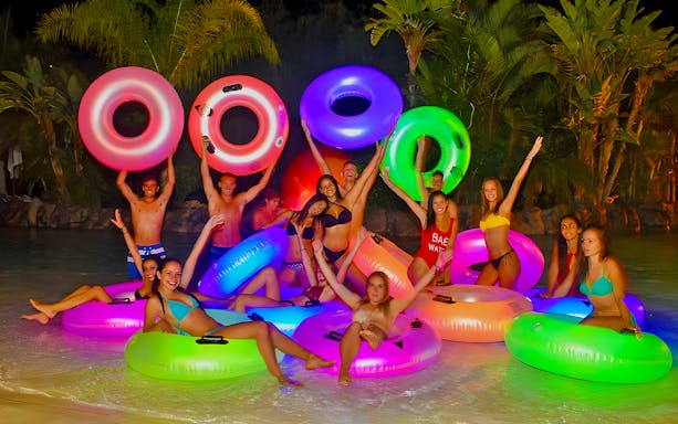 Group of friends enjoying a night ride at Siam Park, illuminated water slide in the background, Tenerife.