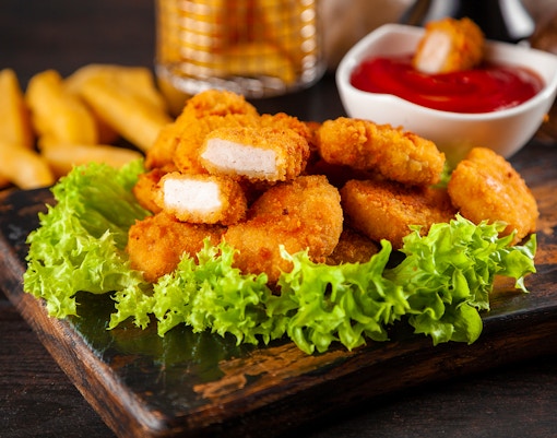 Crispy chicken nuggets on a wooden board with lettuce and dipping sauce.