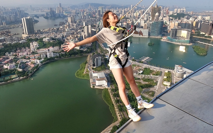 Person bungee jumping at Skypark Macau by AJ Hackett with cityscape view.