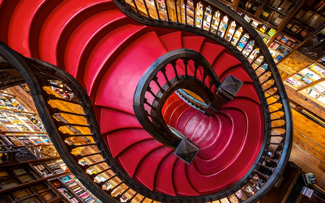 Spiral staircase at Lello Library in Porto, Portugal, surrounded by bookshelves.