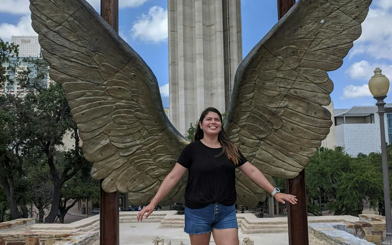 Person posing with large wing sculpture in San Antonio during city exploration game.