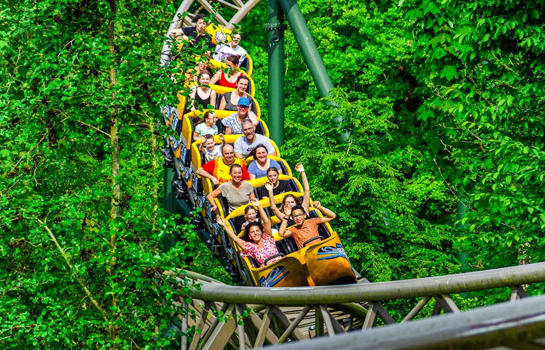 People enjoying a ride on a boomerang roller coaster surrounded by lush greenery.