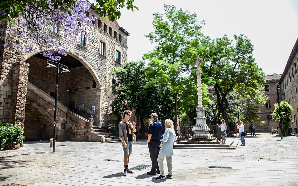 Tour group in Raval, Barcelona, near historic stone arch and ornate column.