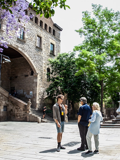 Tour group in Raval, Barcelona, near historic stone arch and ornate column.