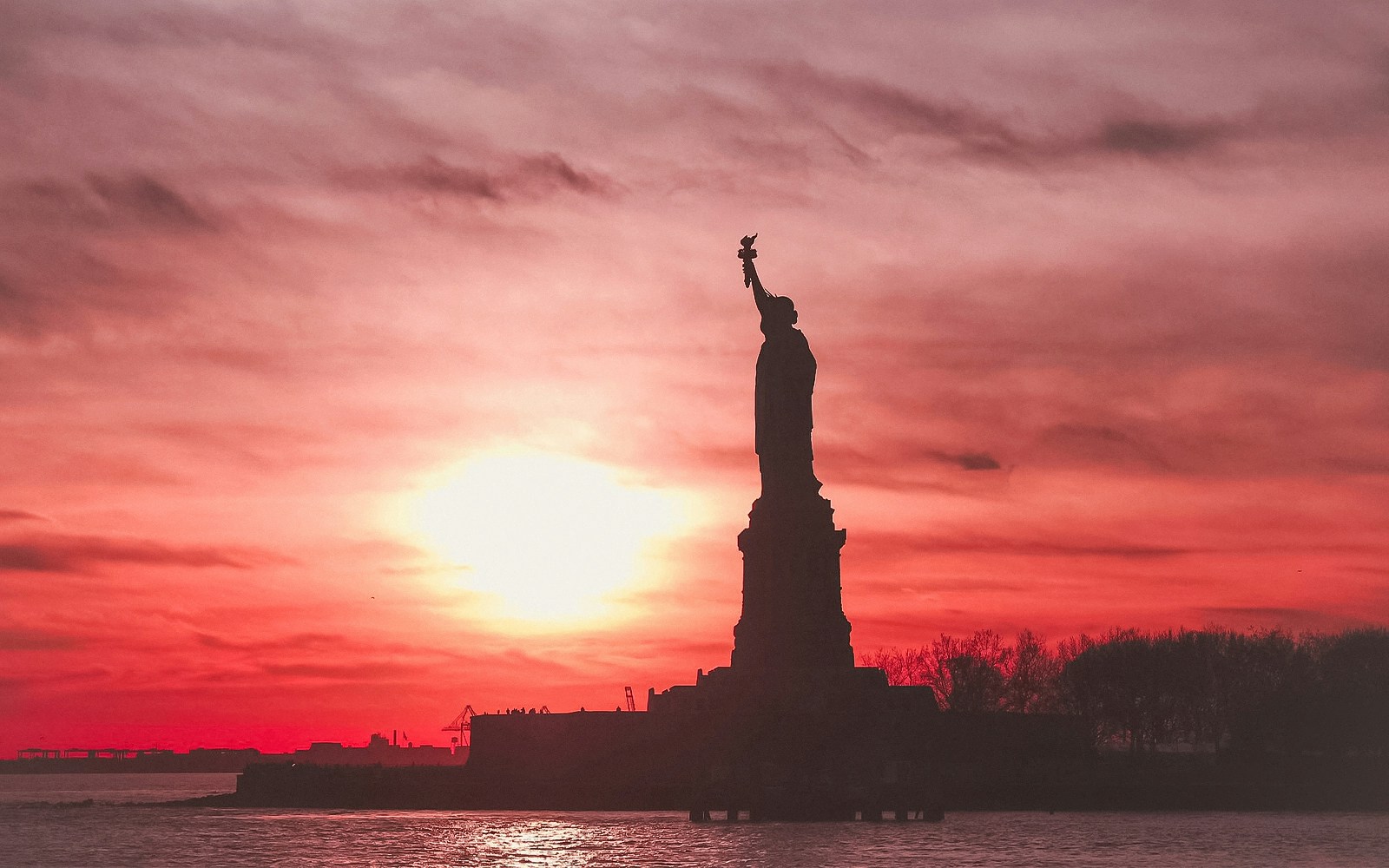 Statue of Liberty and Ellis Island at sunset during a scenic cruise in New York Harbor.