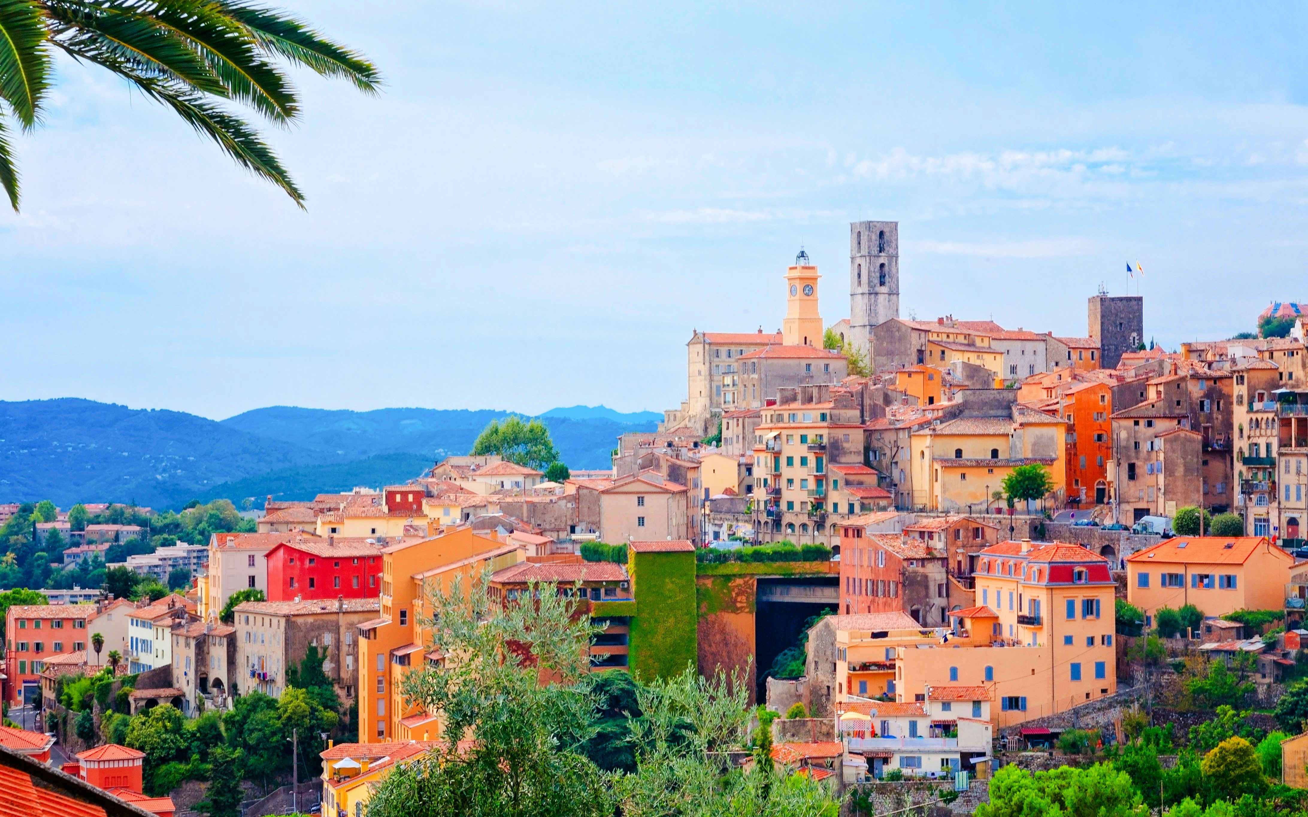 Colorful hillside buildings in Grasse, France with distant mountains.