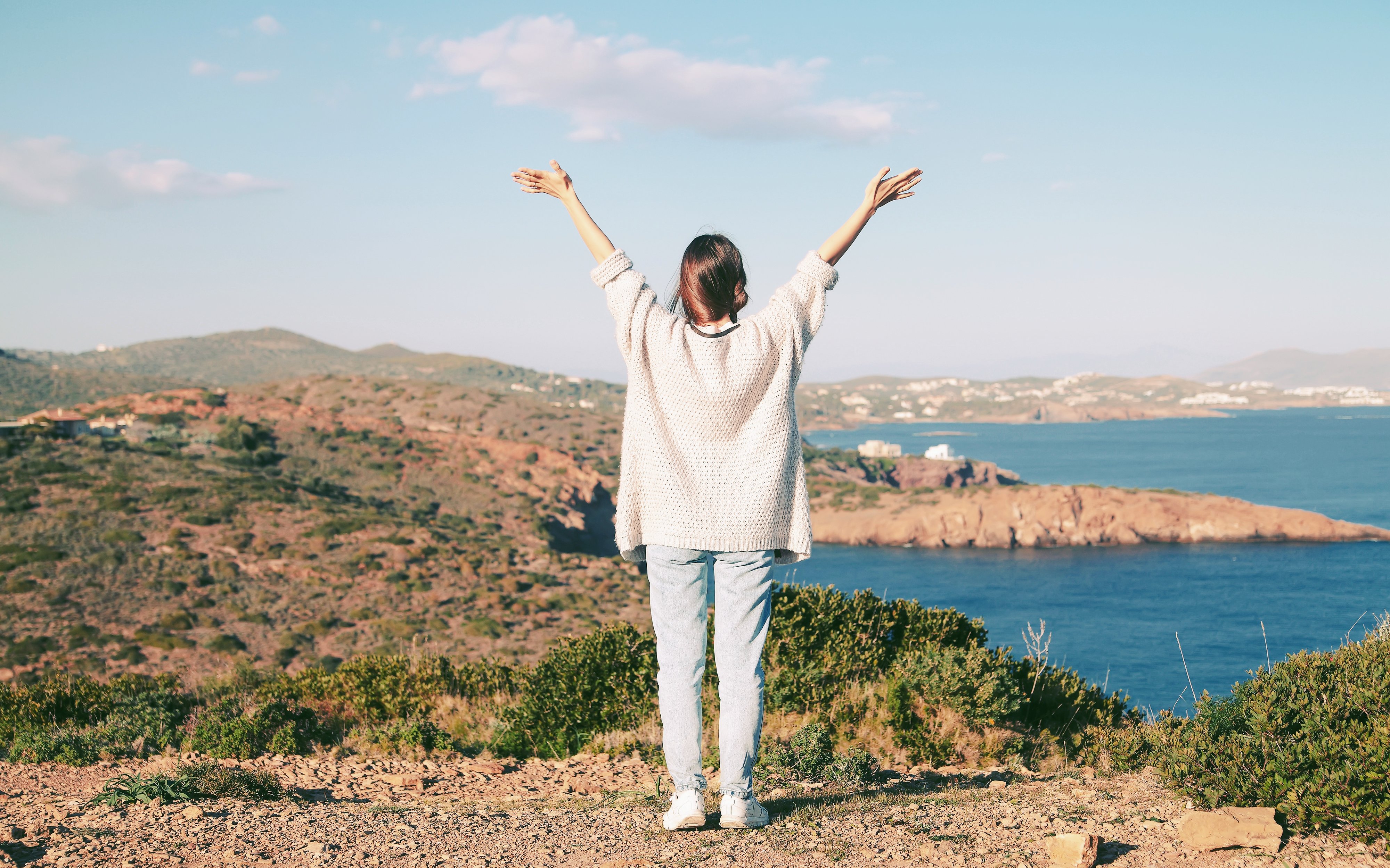 Woman with arms raised on Cape Sounion cliff overlooking the Aegean Sea, Greece.