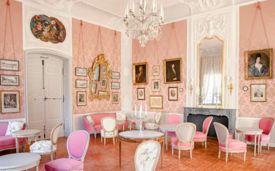 Elegant interior of Caumont Centre d’Art with pink walls, ornate mirrors, and classic paintings.