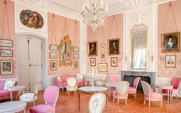 Elegant interior of Caumont Centre d’Art with pink walls, ornate mirrors, and classic paintings.