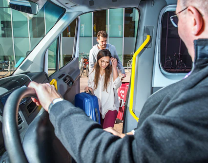 Passengers boarding a van with luggage at a city location.