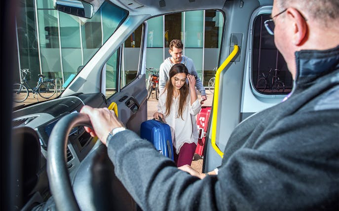 Passengers boarding a van with luggage at a city location.