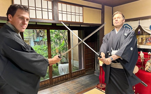 Two men in traditional attire posing with swords in a Japanese room.