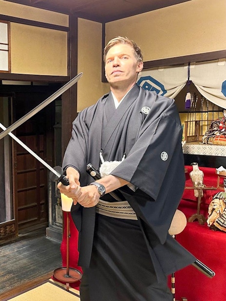 Two men in traditional attire posing with swords in a Japanese room.