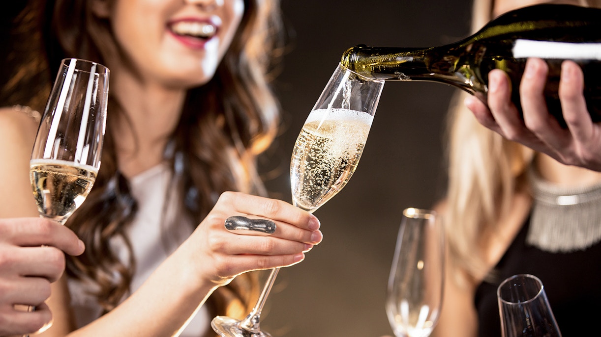 Barista pouring Champagne into a glass at a social gathering.