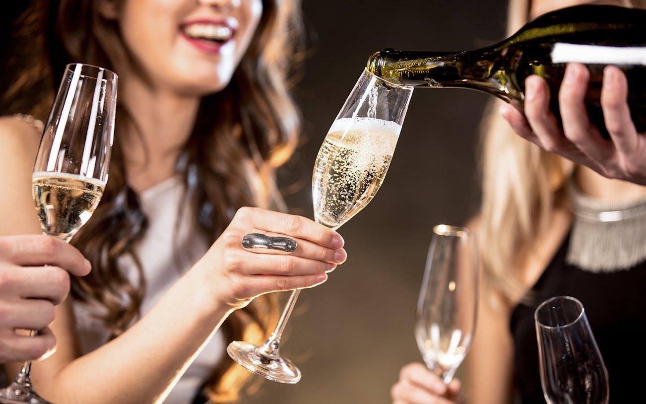 Barista pouring Champagne into a glass at a social gathering.