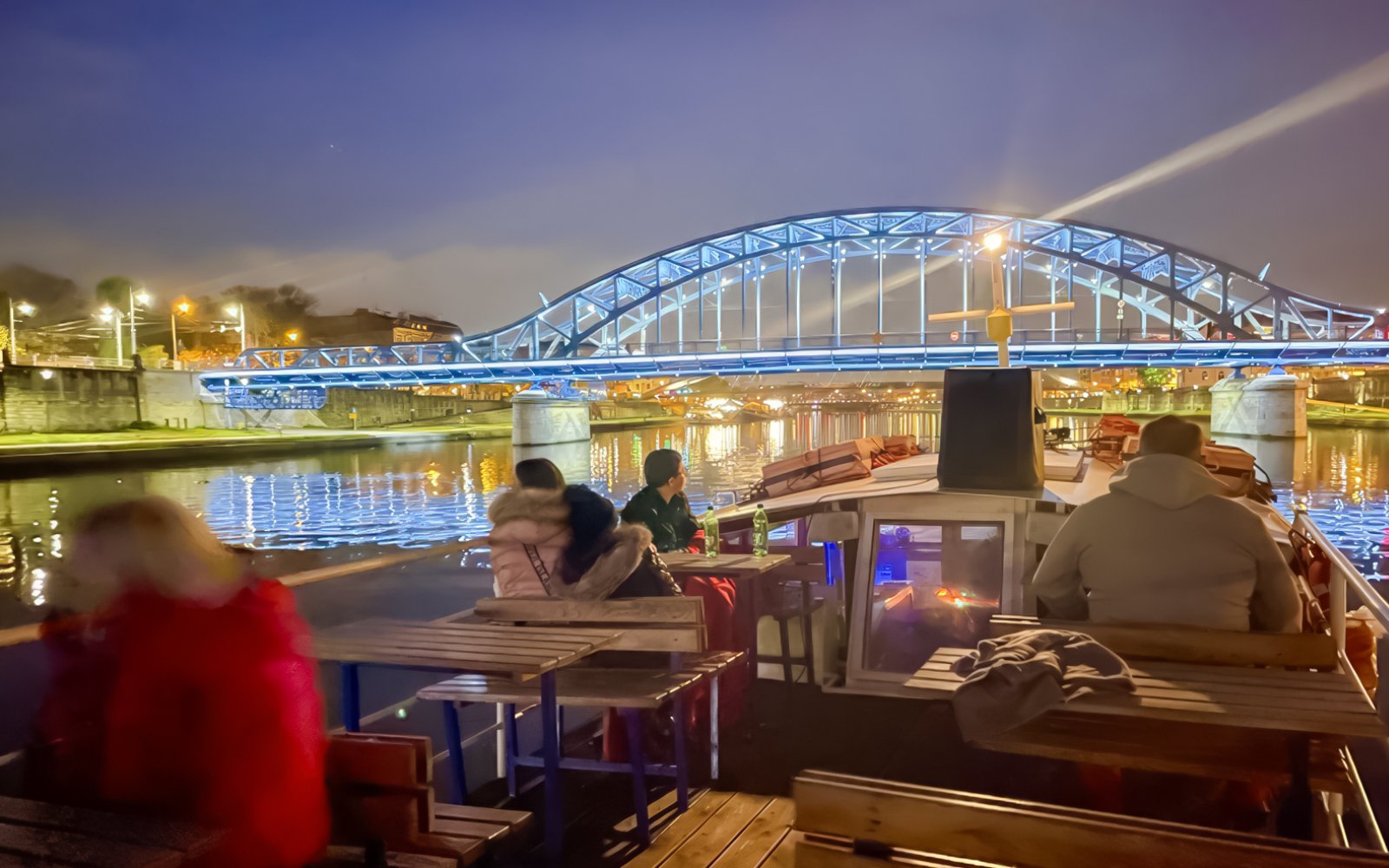 Guests enjoying a night cruise on the Vistula River with a lit bridge in the background.