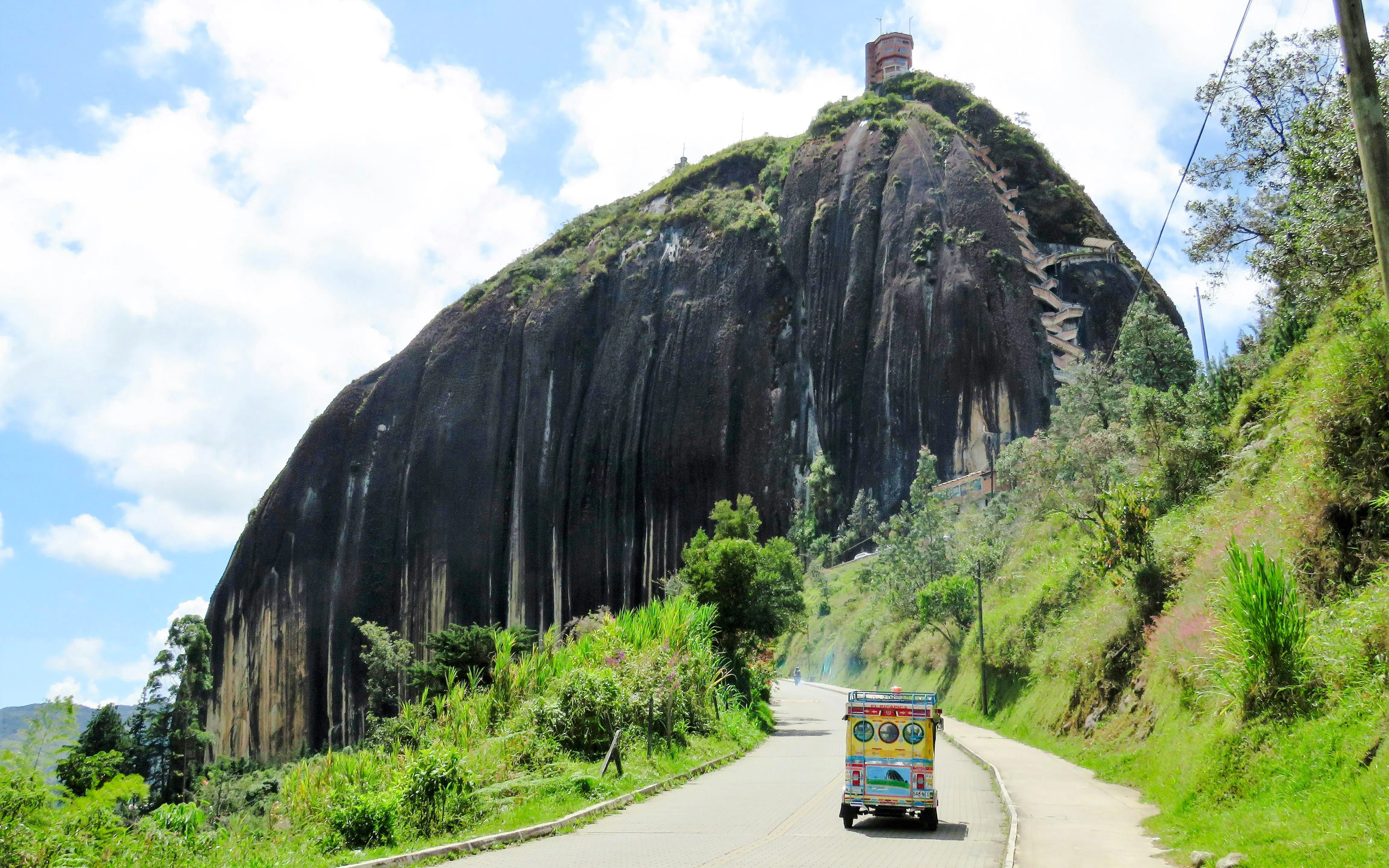 Chiva bus approaching La Piedra de Guatapé rock formation in Colombia.