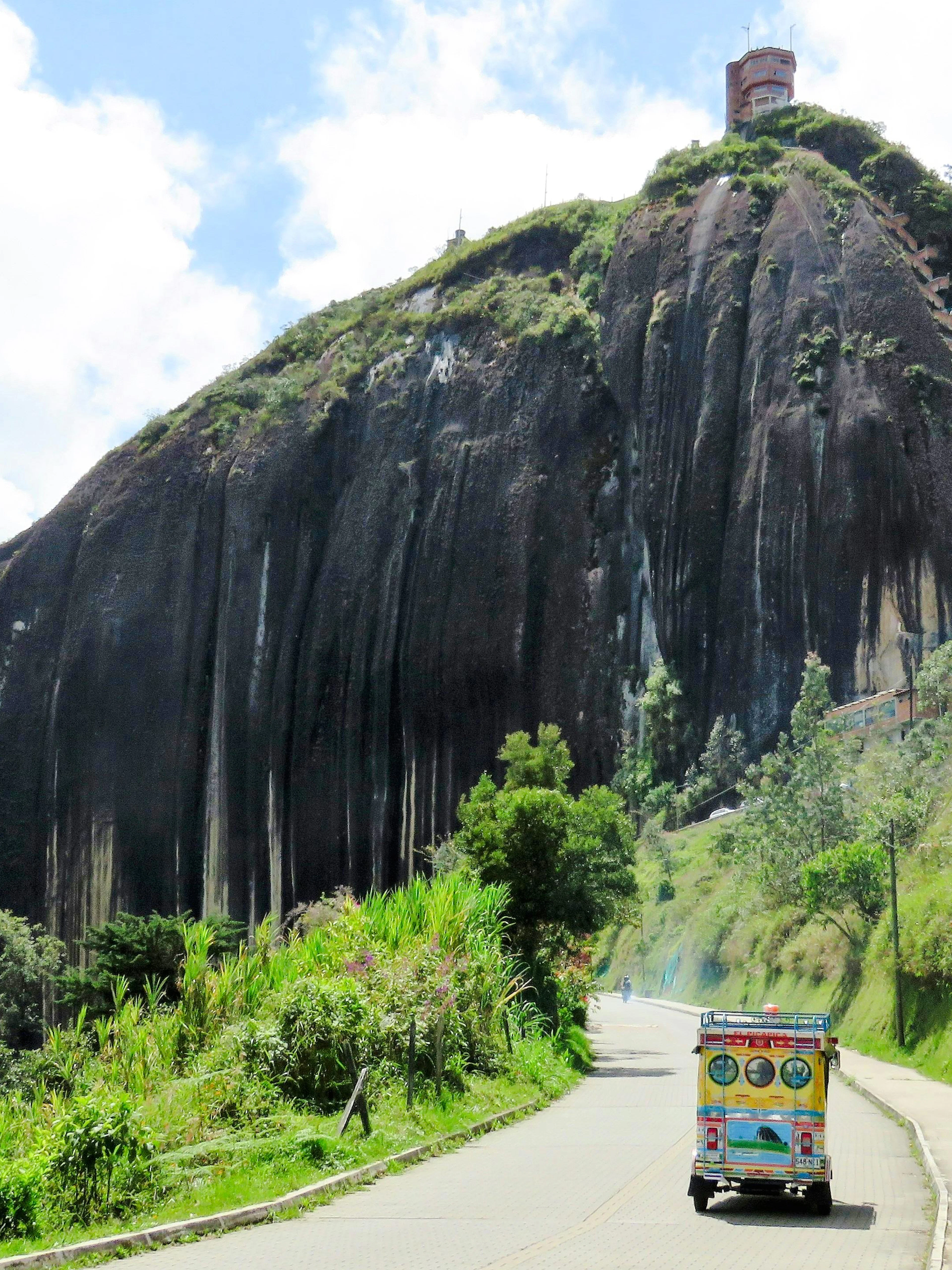 Chiva bus approaching La Piedra de Guatapé rock formation in Colombia.